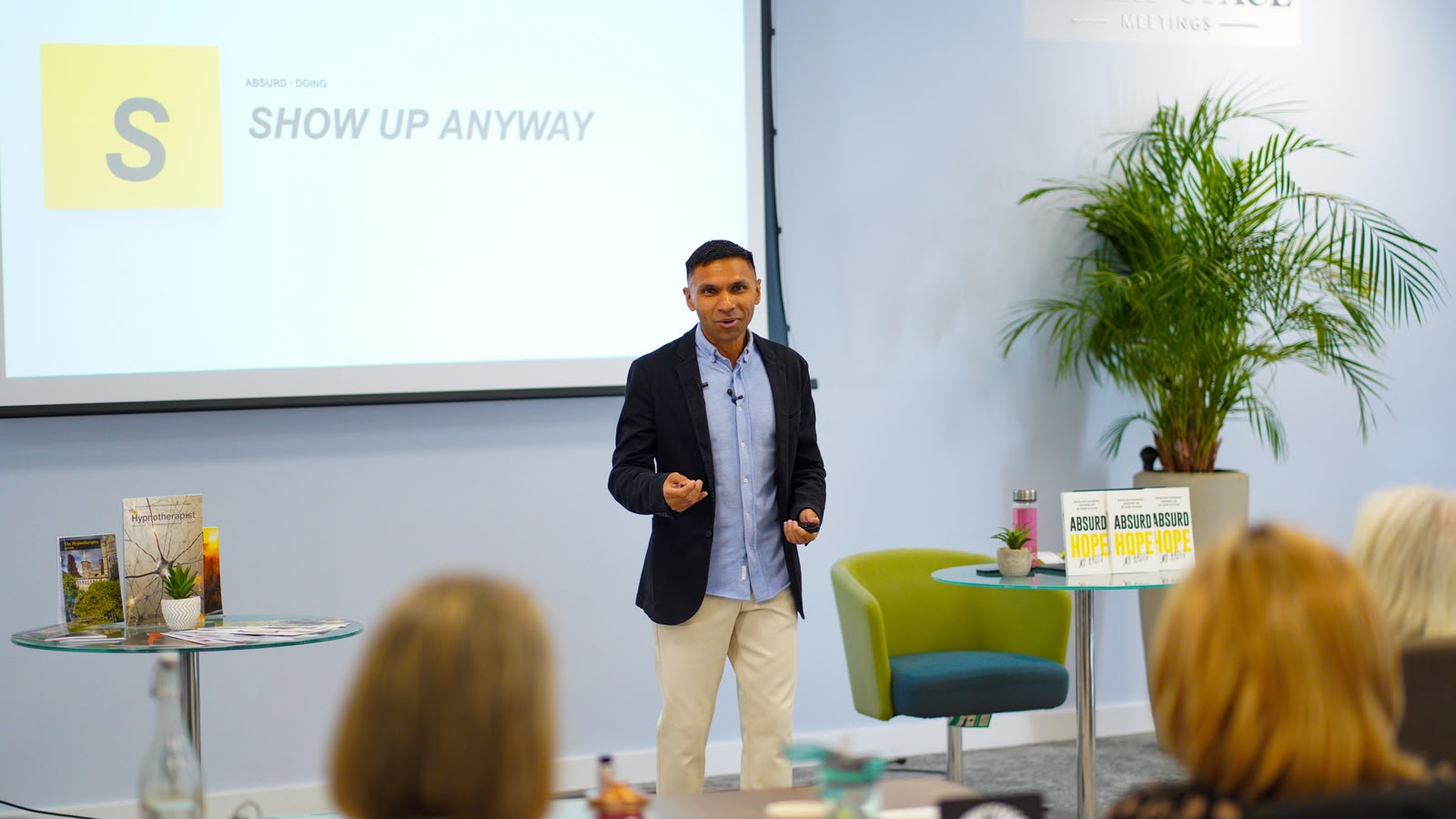 Mo Haque on stage with the Absurd Hope book — Show Up Anyway
